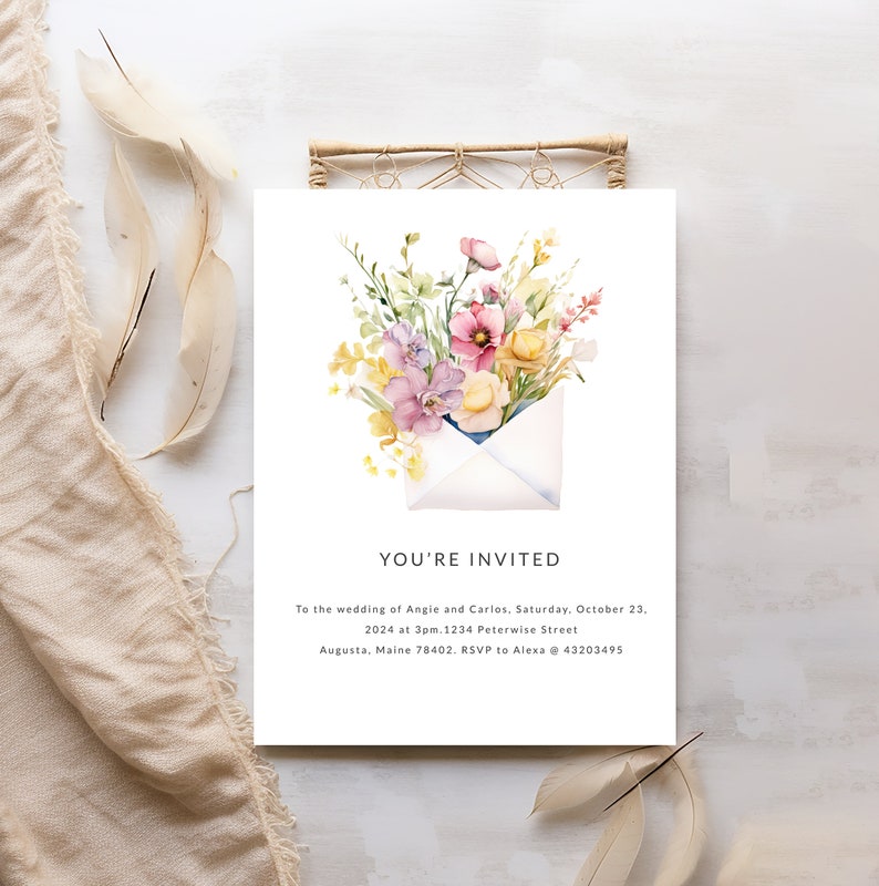 May include: A wedding invitation featuring a watercolour illustration of a white envelope with a bouquet of pink, yellow, and purple flowers inside. The text reads "You're Invited" and includes the wedding details: Angie and Carlos, Saturday, 23rd October, 2024 at 3pm, 1234 Peterwise Street, Augusta, Maine 78402. RSVP to Alexa @ 43203495.