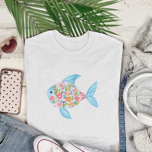 White t-shirt with a floral fish graphic, styled with jeans, headphones, and sunglasses.