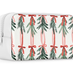 K&ouml;nnte beinhalten: Wei&szlig;e Kosmetiktasche mit Rei&szlig;verschluss und einem sich wiederholenden Muster aus gr&uuml;nen Kiefernzweigen, die mit roten und rosa B&auml;ndern gebunden sind.