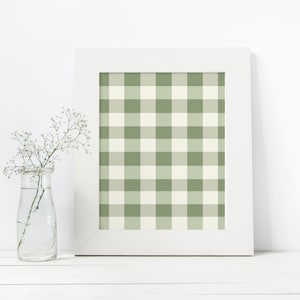 May include: A white picture frame with a green and white gingham pattern inside. The frame is sitting on a white surface with a clear glass vase with white flowers.