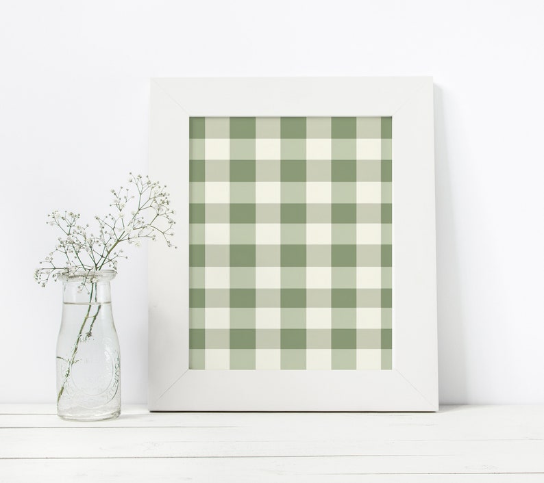 May include: A white picture frame with a green and white gingham pattern inside. The frame is sitting on a white surface with a clear glass vase with white flowers.