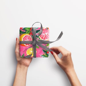 May include: A pink gift box with a gray ribbon tied in a bow. The box is wrapped in paper with a pattern of lemons, limes, and grapefruits.