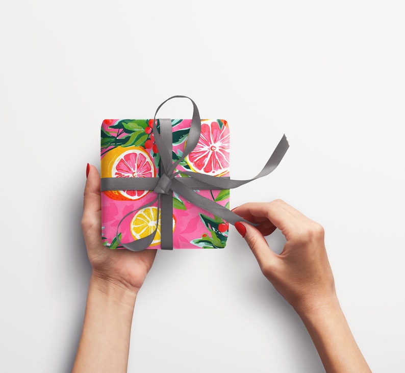 May include: A pink gift box with a gray ribbon tied in a bow. The box is wrapped in paper with a pattern of lemons, limes, and grapefruits.