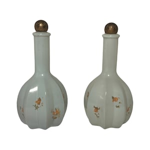 Pode incluir: Duas garrafas de vidro branco com tampas douradas e desenhos florais. As garrafas têm um design nervurado e são em forma de bulbo.