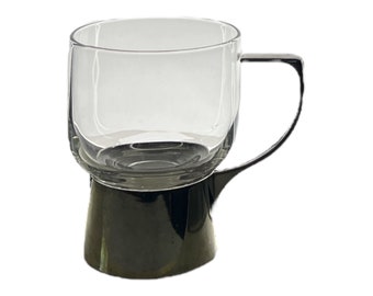 Op de afbeelding: Een heldere glazen mok met een zwarte basis en een zwarte handgreep. De mok heeft een afgeronde vorm en een brede basis.