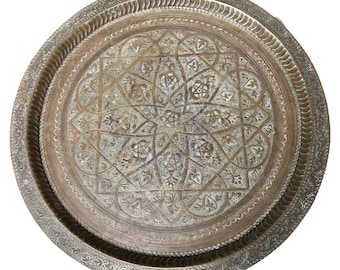 May include: A round, brass serving tray with an intricate, embossed design. The tray has a raised rim and a decorative border.