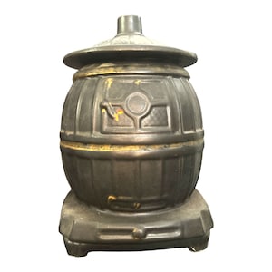 Puede incluir: Un tarro de galletas de cerámica negra con forma de estufa de leña con ribete dorado. La tapa tiene forma de chimenea.