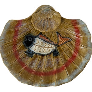 以下が含まれることがあります： 茶色、白、赤、黒のスタイリッシュな魚のデザインが施された、貝殻の形をしたセラミック製の皿。皿は釉薬仕上げで、表面はテクスチャ加工されています。