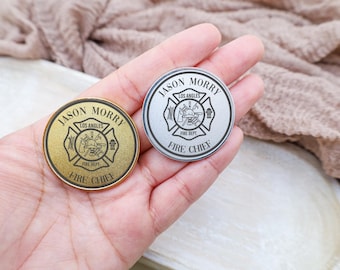 May include: Two round metal challenge coins with the text "Jason Morry" and "Los Angeles Fire Dept. Fire Chief" engraved on them. One coin is gold and the other is silver.