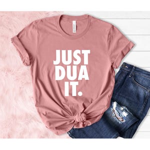 May include: A dusty rose t-shirt with the text "JUST DUA IT." printed in white.