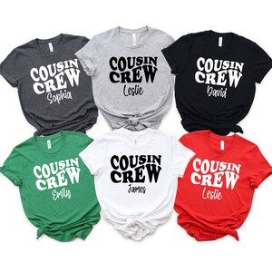 May include: Six t-shirts in different colors with the text "COUSIN CREW" in a retro font and a name underneath. The colors are green, red, white, black, gray, and heather gray.
