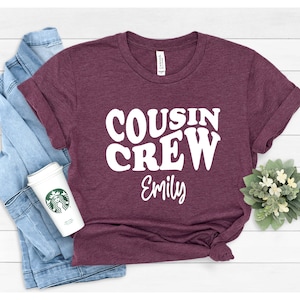 May include: A maroon t-shirt with white text that reads "COUSIN CREW Emily".