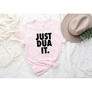 May include: Pink t-shirt with the text "JUST DUA IT." printed in black.