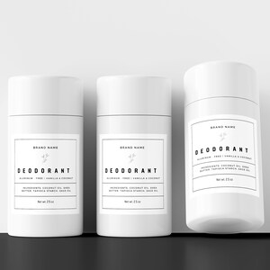 May include: Three white deodorant sticks with black labels. The labels read "BRAND NAME" and "DEODORANT ALUMINUM FREE | VANILLA & COCONUT" with a small floral design. The ingredients are listed on the label. Each stick is 2.5 oz.