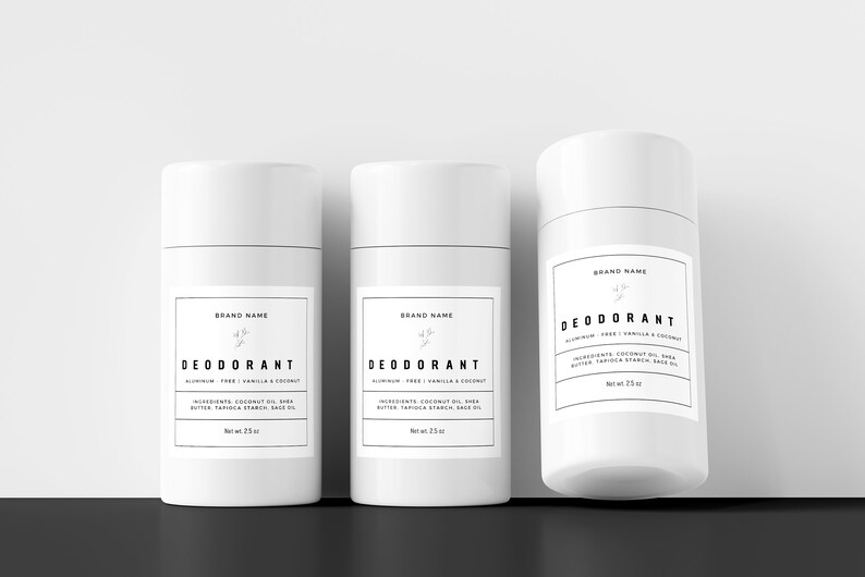 May include: Three white deodorant sticks with black labels. The labels read "BRAND NAME" and "DEODORANT ALUMINUM FREE | VANILLA & COCONUT" with a small floral design. The ingredients are listed on the label. Each stick is 2.5 oz.