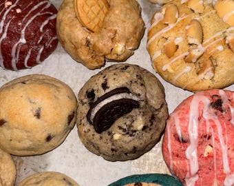May include: An assortment of gourmet cookies, each with unique toppings and flavors. The cookies are various colors, including red, brown, and blue, and are decorated with icing, cookies, and other treats. A delicious treat for any occasion.