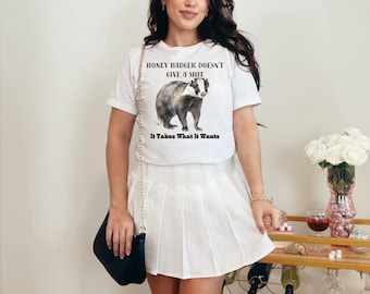 Pode incluir: Camiseta branca com um gráfico de texugo e o texto "Honey Badger Doesn't Give A Shit It Takes What It Wants".