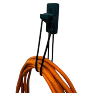 May include: A black cord organizer with a hook for hanging cords. The organizer is mounted to a wall and has a black cord wrapped around it.