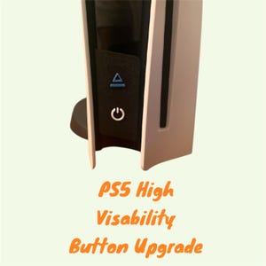 Puede incluir: Primer plano de una consola PlayStation 5 blanca con un panel de botones negro. El panel tiene un botón triangular azul y un botón de encendido blanco. El texto "PS5 High Visability Button Upgrade" está escrito debajo de la consola.