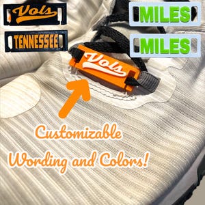May include: White athletic shoes with customizable orange and black shoe laces. The laces have the words "Vols" and "Tennessee" on them. The text "Customizable Wording and Colors!" is written below the shoes.
