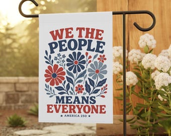 Puede incluir: Una bandera de jardín blanca con el texto en rojo y azul WE THE PEOPLE MEANS EVERYONE y el texto pequeño AMERICA 250 entre dos estrellas. El diseño incluye un arreglo floral central con flores rojas, azul oscuro y azul claro.
