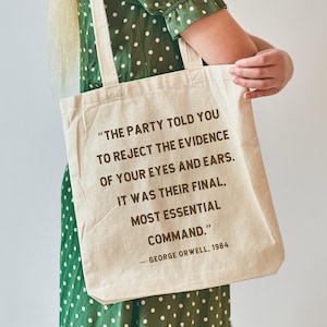 May include: Cream-colored tote bag with the quote "THE PARTY TOLD YOU TO REJECT THE EVIDENCE OF YOUR EYES AND EARS. IT WAS THEIR FINAL, MOST ESSENTIAL COMMAND." by George Orwell, 1984. The bag has two handles and is held by a person.