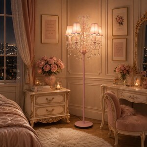 May include: A pink floor lamp with a crystal chandelier design in a bedroom. The room features a nightstand, a vanity, and a bed, all in a similar pink and cream colour scheme. The room is decorated with flowers and framed artwork.