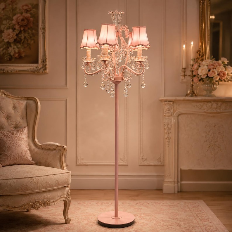 May include: A pink chandelier floor lamp with four shades. The lamp has a crystal design and a round base. The lamp is in a room with a chair, a painting, and a fireplace.
