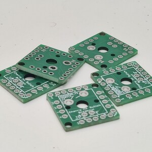 May include: A collection of green square circuit boards with multiple holes and text that reads "Cherry mx Switch Breakout". The boards are arranged in a slightly overlapping pattern, with a white background.