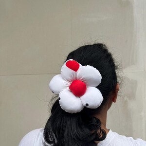 A white flower scrunchie with a red center and black polka dots. The flower is attached to a black ponytail. The hair accessory is worn on the back of a person's head, against a neutral background. Handmade Fluffy Floral Scrunchie: Long Hair Tie