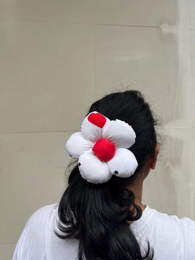 A white flower scrunchie with a red center and black polka dots. The flower is attached to a black ponytail. The hair accessory is worn on the back of a person's head, against a neutral background. Handmade Fluffy Floral Scrunchie: Long Hair Tie