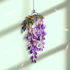 Pu&ograve; includere: Un acchiappasole a forma di glicine in vetro colorato con fiori viola, lavanda e rosa e foglie verdi. Il pezzo decorativo floreale &egrave; appeso a una catena e presenta dettagli iridescenti. Una decorazione floreale per finestre o pareti.