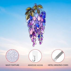 Pu&ograve; includere: Decorazione da appendere in vetro colorato a forma di glicine. Presenta petali viola, blu e rosa e foglie verdi. Include un gancio adesivo e una catena di metallo per appenderla.