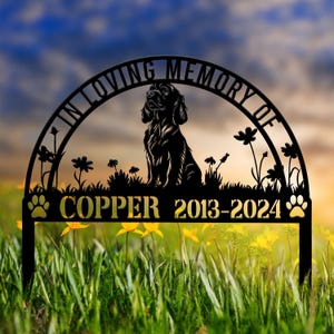 Könnte beinhalten: Schwarzer Metall-Gedenk-Gartenpfahl mit einer Silhouette eines Hundes, der in einem Blumenfeld sitzt. Der Pfahl trägt die Aufschrift "In Loving Memory Of" und "Copper 2013-2024" mit Pfotenabdrücken auf beiden Seiten.