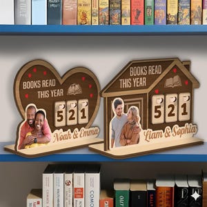May include: Wooden book-themed decor pieces. One is heart-shaped, the other a house, both with the text "BOOKS READ THIS YEAR" and a counter showing "521". Each has a photo of a couple and the names "Noah & Emma" and "Liam & Sophia".