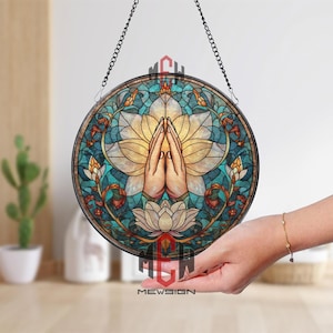 Puede incluir: Arte de ventana de vidriera redonda con una flor de loto y manos en oración. El diseño incorpora tonos turquesa, amarillo y naranja, con una cadena negra para colgar. Incluye el texto "MEWSIGN".