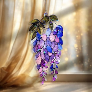 Pu&ograve; includere: Un acchiappasole a vetrata con un design a glicine. Presenta grappoli di vetro a forma di petalo viola, blu e rosa, con foglie verdi e dorate nella parte superiore. Progettato per catturare la luce.