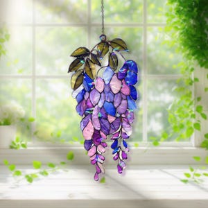 Pu&ograve; includere: Una decorazione a sospensione in vetro colorato a forma di glicine. Il pezzo presenta una cascata di pezzi di vetro a forma di petalo viola, blu e rosa, con foglie verdi e dorate. Appeso a una delicata catena.