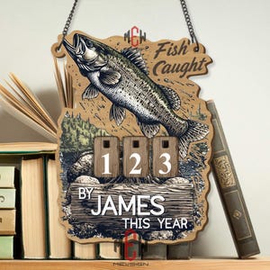 Puede incluir: Cartel de madera con una ilustración de un pez y las palabras "Fish Caught". Cuenta con un contador con los números 1, 2 y 3, y el texto "By James This Year". El cartel está diseñado para colgarse.