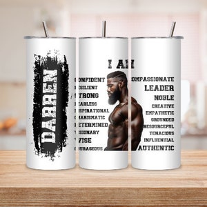 Op de afbeelding: Een witte tumbler met een zwart-wit ontwerp met de naam "DARREN" en een lijst met positieve eigenschappen. De tumbler staat naast een vergelijkbare tumbler met een portret van een zwarte man en een lijst met positieve eigenschappen. De tekst op de tumbler luidt "I AM COMPASSIONATE LEADER NOBLE CREATIVE EMPATHETIC GROUNDED RESOURCEFUL TENACIOUS INFLUENTIAL AUTHENTIC".