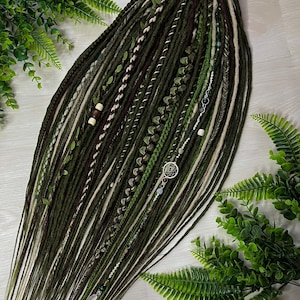 May include: A set of dark green and white dreadlocks with decorative elements. The dreadlocks are in various shades of green, brown, and white, with leaf and bead embellishments. A silver dreamcatcher charm is also included.