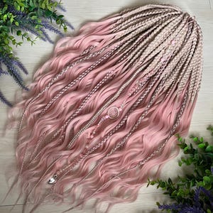 May include: A set of synthetic hair extensions featuring a blend of light pink and beige tones. The hair consists of a combination of tight braids and loose, wavy strands. Decorative elements include small beads and a circular charm accessory.