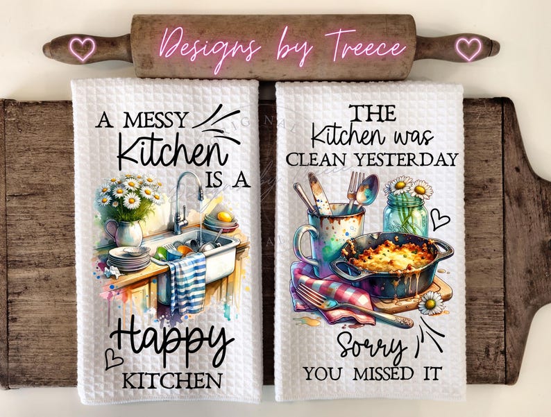 May include: Two white kitchen towels with watercolor illustrations and text. One towel reads "A Messy Kitchen is a Happy Kitchen" with a sink scene. The other says "The Kitchen was Clean Yesterday, Sorry You Missed It" with a food scene.