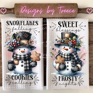 May include: Two white waffle-weave kitchen towels with snowman designs. One towel reads "Snowflakes falling, Cookies calling" and the other reads "Sweet blessings, Frosty nights." Each snowman wears a top hat, scarf, and mittens, holding a gingerbread cookie.