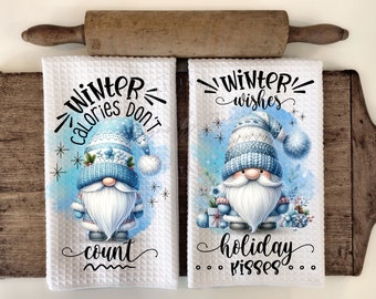 Könnte beinhalten: Zwei weiße Waffel-Küchentücher mit Zwergenmotiven. Auf einem Handtuch steht "Winter calories don't count" und auf dem anderen "Winter wishes holiday kisses". Die Zwerge tragen blaue Hüte und Mäntel.