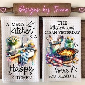 May include: Two white kitchen towels with watercolor illustrations and text. One towel reads "A Messy Kitchen is a Happy Kitchen" with a sink scene. The other says "The Kitchen was Clean Yesterday, Sorry You Missed It" with a food scene.