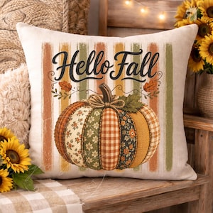 Op de afbeelding: Een vierkant sierkussen met een crèmekleurige achtergrond en verticale strepen in gedempt oranje, geel en groen. De tekst "Hello Fall" is in zwarte letters gedrukt boven een grote centrale pompoenafbeelding met diverse stofpatronen.