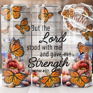 Può includere: Un bicchiere bianco con un motivo a venature di legno presenta un design a farfalla e il testo "But the Lord stood with me and gave me Strength 2 Timothy 4:17".