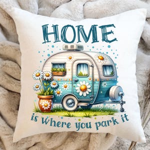 以下が含まれることがあります： 白い枕に、青と白のキャンピングカーのイラストと「HOME is where you park it」というテキストが書かれています。キャンピングカーにはデイジーが描かれており、デイジーの入った鉢植えの前に駐車されています。