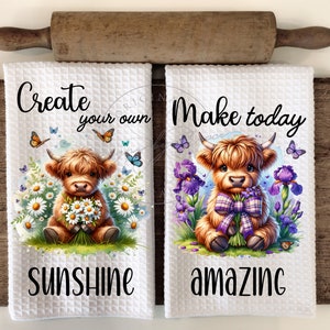 May include: Two white kitchen towels with a cute Highland cow design. The first towel says "Create your own sunshine" and the second towel says "Make today amazing".
